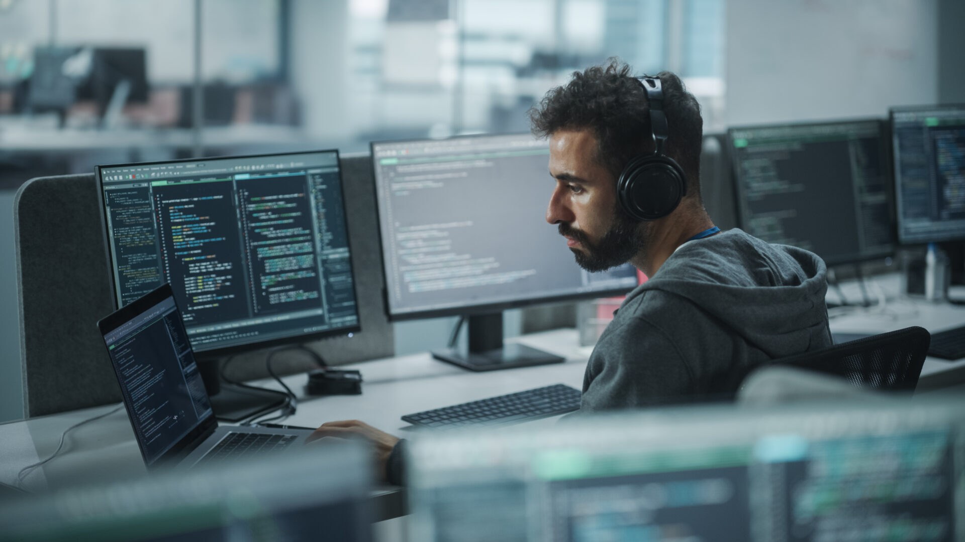Office: Professional White IT Programmer Uses Headphones while Working on Desktop Computer. Male Website Developer, Software Engineer Developing App, Video Game. Listening to Podcast, Music.